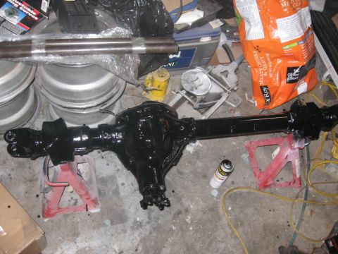 1988 Ford Bronco - A black rear axle assembly is supported by red jack stands amidst various automotive parts and supplies.