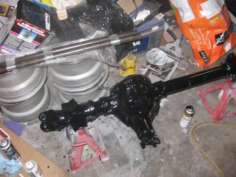 1988 Ford Bronco - A freshly painted rear axle assembly sits on jack stands, surrounded by parts and tools, suggesting a vehicle repair or upgrade project.