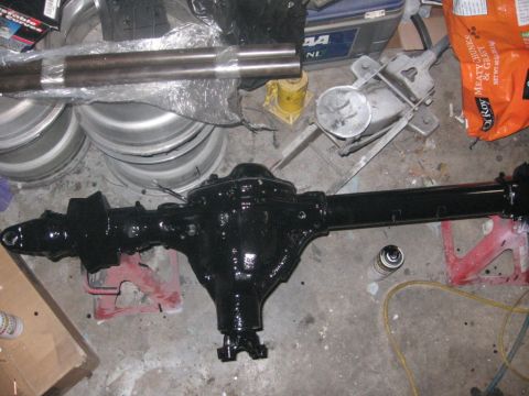 1988 Ford Bronco - A freshly painted rear axle assembly is shown with spare wheels and other automotive parts in a garage setting.