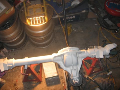 1988 Ford Bronco - A differential axle assembly is shown on jack stands in a workshop setting, with various tools and tires nearby.