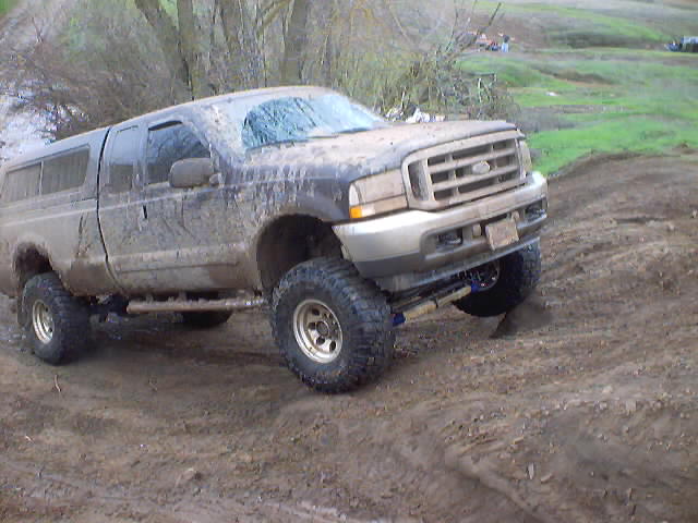 Muddy Ford Super Duty pickup truck with a camper shell, lifted with large tires, driving on a dirt track