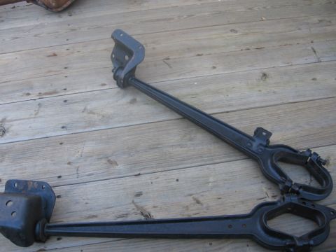 1988 Ford Bronco - Two black metal suspension components are laid out on a weathered wooden deck.