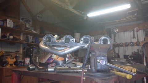 1995 Ford Bronco - Custom exhaust headers are being worked on in a garage setting, with tools and shelves in the background.