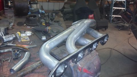 1995 Ford Bronco - Custom exhaust headers are shown clamped in a vise on a workbench, surrounded by tools and parts.