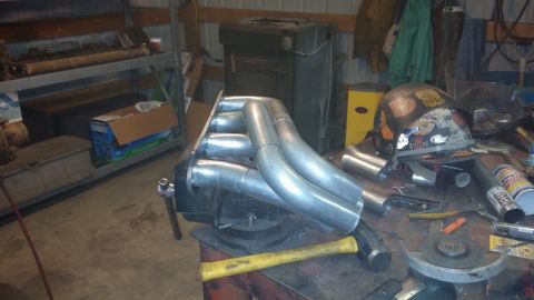 1995 Ford Bronco - Custom exhaust headers are held in a vise on a cluttered workbench.