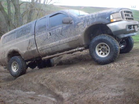 1976 Ford F-100 - A dark-colored Ford F-Series truck is covered in mud while driving on a dirt path.