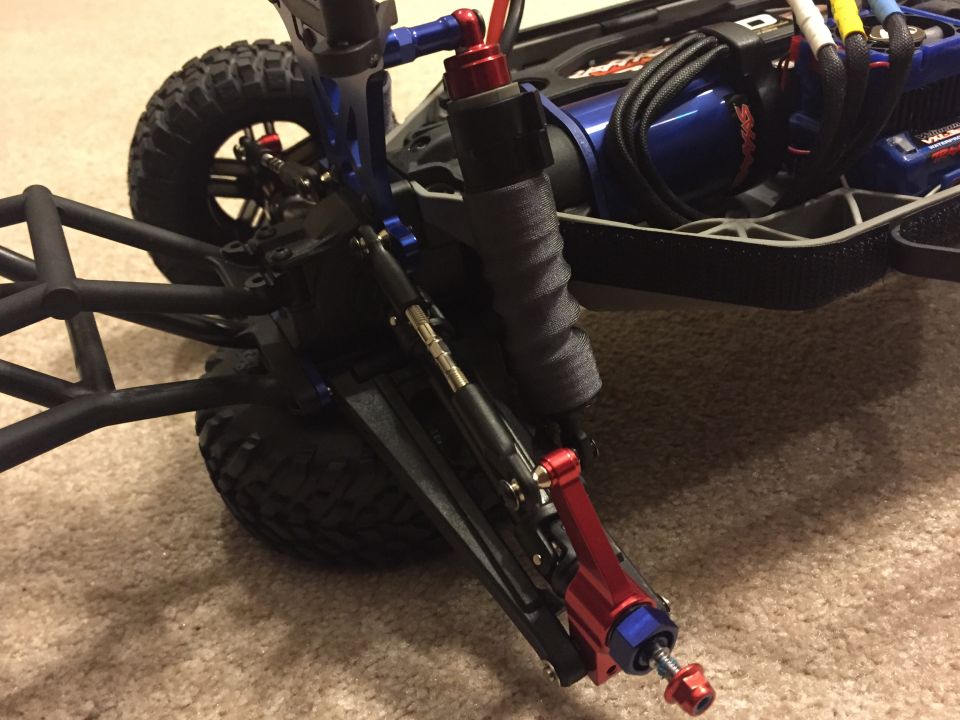 RC car front suspension with blue and red aluminum parts, black roll cage, and knobby tires on carpet