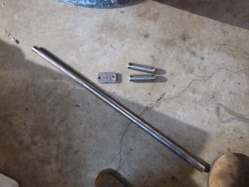 Metal rod with two small cylindrical pieces and a rectangular bracket on a concrete floor