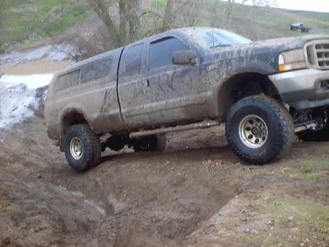 1976 Ford F-100 - A lifted pickup truck navigates a muddy off-road trail, with another vehicle visible in the background.