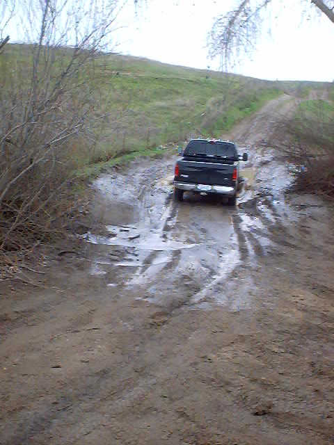 1976 Ford F-100 - A black pickup truck navigates a challenging muddy path with standing water.