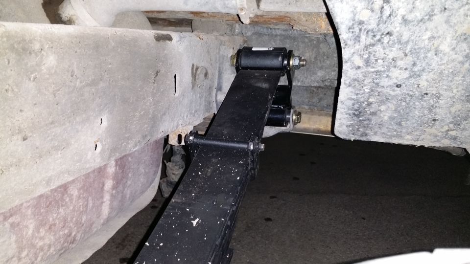 Close-up of a leaf spring attached to a vehicle frame with new bushings