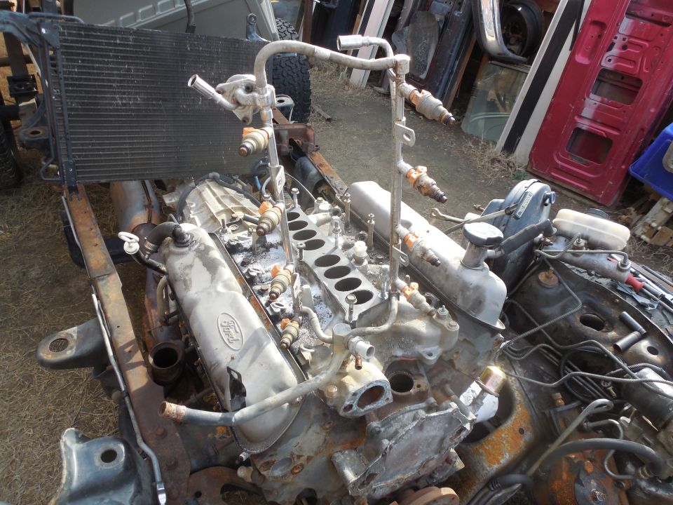 Disassembled Ford inline engine with exposed head and fuel rail in a junkyard