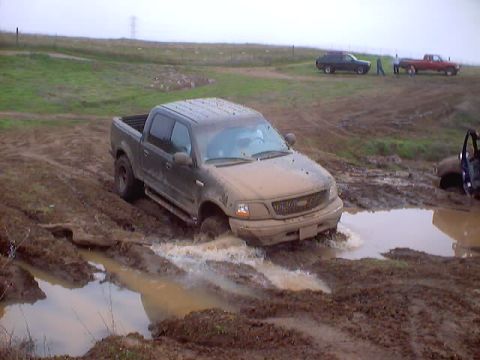 1976 Ford F-100 - A pickup truck struggles through a muddy off-road course with other vehicles visible in the background.
