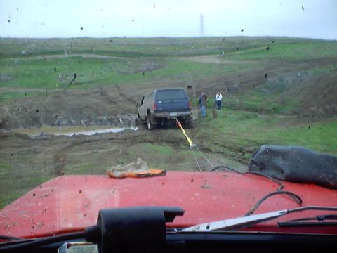 1976 Ford F-100 - A vehicle is being towed out of a muddy ditch on a cloudy day.