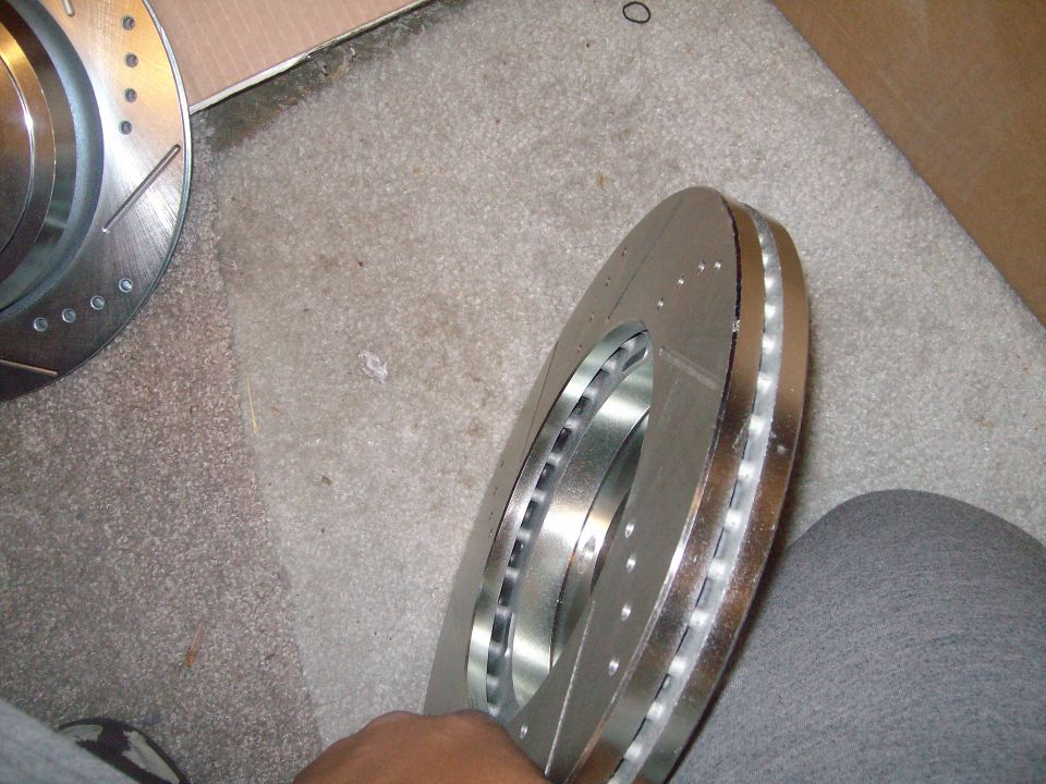 Two new slotted and drilled brake rotors, one held by a hand