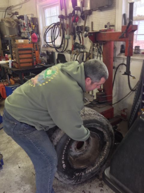 1979 Ford Bronco - A person is shown in a garage, focused on changing a tire with various tools in the background.