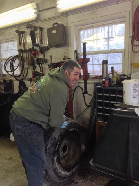 1979 Ford Bronco - A man works on a tire in a cluttered garage with tools on the wall.