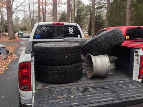 1979 Ford Bronco - A white pickup truck bed is filled with several tires and rims, with a red truck partially visible in the background.