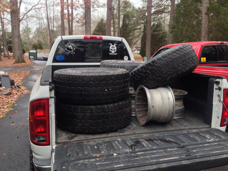 Pickup truck bed loaded with tires and rims, red truck visible