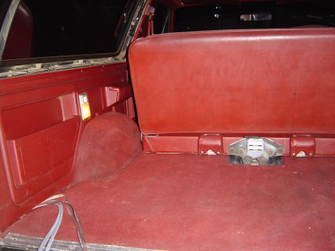 1986 Ford Bronco - Red interior of an SUV showing the rear cargo area with red carpeting and a folded/removable red vinyl rear bench seat back, with a metal s…