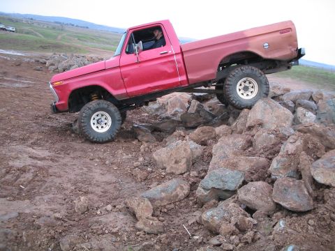 1976 Ford F-100 - A red pickup truck navigates a rocky terrain, its tires gripping the uneven surface.