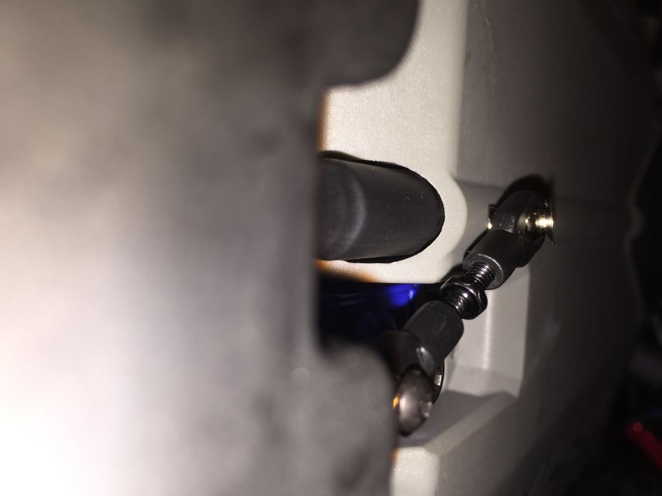 Close-up of an adjustable linkage with black rod ends and a threaded shaft, attached to a gray housing