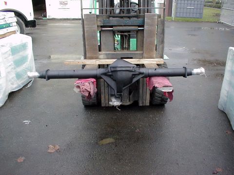 1983 Ford Bronco - A rebuilt solid axle housing painted flat black, shown end-on across a forklift's forks with red rags padding the tubes and plastic taped o…