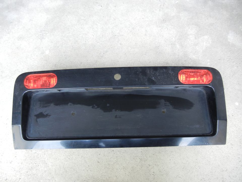 Black license plate bezel with two red lights. Has a spot for a license plate and a circular hole above it