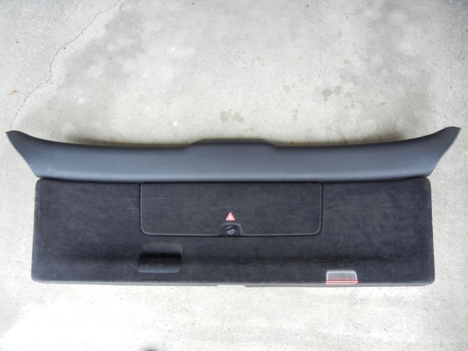 Dark gray plastic trim piece above a black fabric-covered panel with a small storage compartment and a red triangle warning reflector