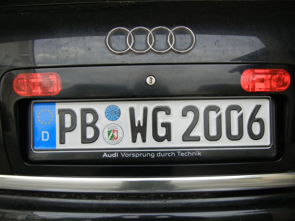 Rear of a car showing the Audi rings badge and a German license plate PB WG 2006. The plate frame has 'Audi Vorsprung durch Technik' text