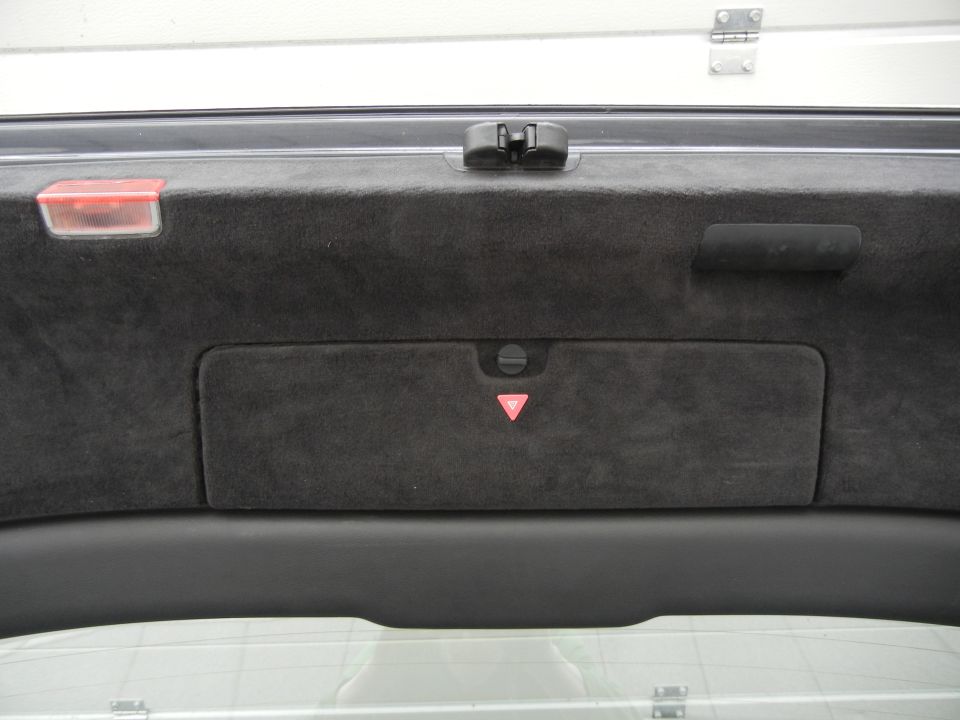 Car trunk interior with black carpet lining, a red reflector, and a warning triangle emblem