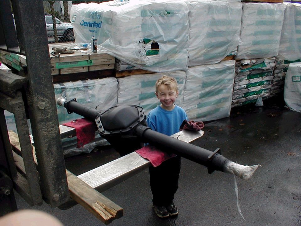 Freshly painted black solid axle housing on wood cribbing with a child standing behind