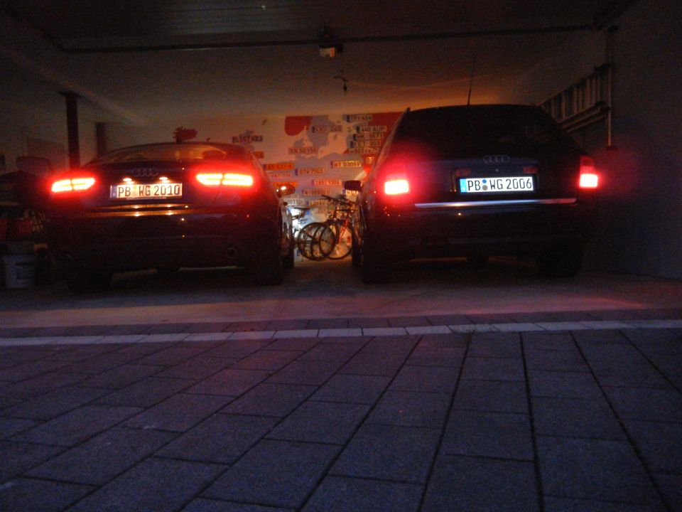 Rear view of two dark sedans, one with license plate PB WG 2010 and the other PB WG 2006, parked in a garage