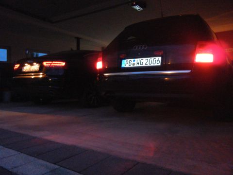 2003 Audi A6 - Two dark sedans are parked, with the rear of one prominently displaying the license plate PB WG 2006.