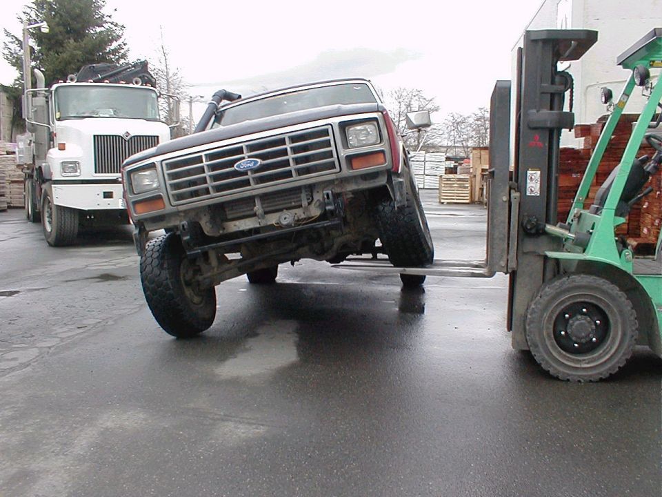 Dark red Ford Bronco with snorkel, lifted, being moved by a forklift. A white truck is in the background
