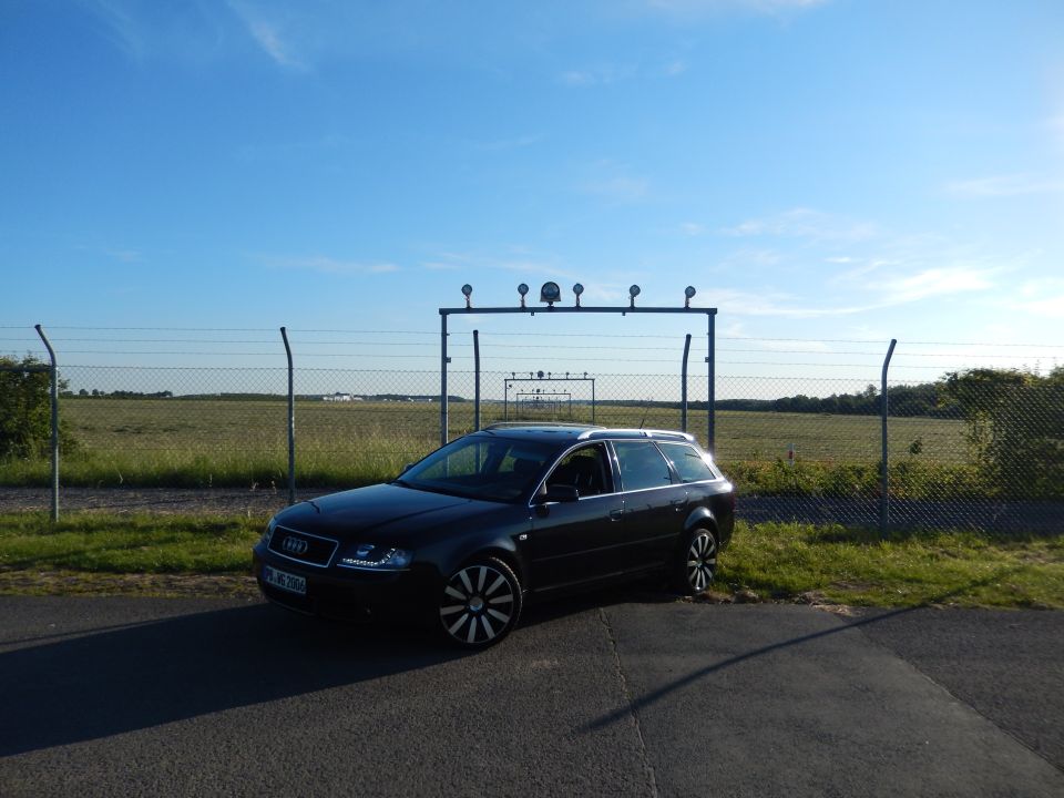 Black Audi A6 Avant parked on asphalt, 3/4 front view, clear sky