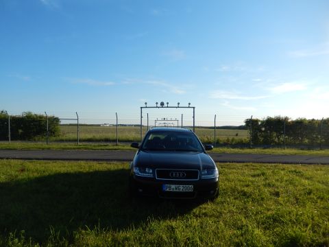 2003 Audi A6 - Black Audi sedan with license plate PB-WG 2006 parked on grass near an airport fence.
