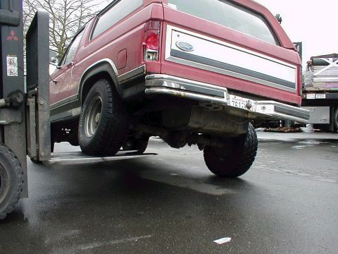 1983 Ford Bronco - Forklift lifts the rear of a red 1983 Ford Bronco. License plate 761LW is visible.