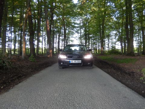 2003 Audi A6 - A black Audi sedan is viewed head-on from a paved road surrounded by trees.