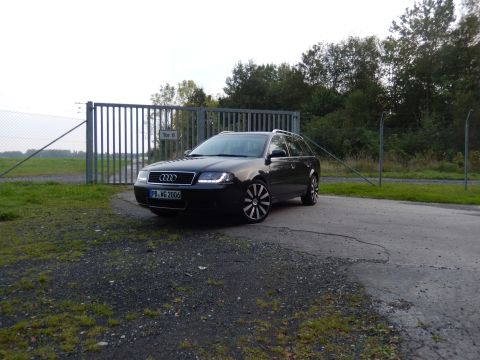 2003 Audi A6 - A dark gray Audi A6 Avant is parked in front of a large metal gate, with trees and a field in the background.