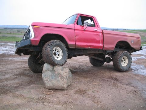 1976 Ford F-100 - A red pickup truck with off-road tires is positioned with its front tire resting on a large rock.