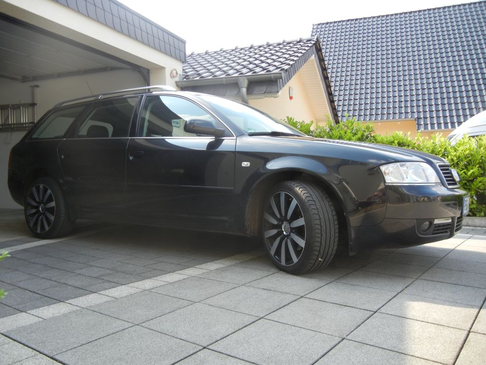 Black station wagon parked in driveway, front quarter view. Aftermarket wheels visible