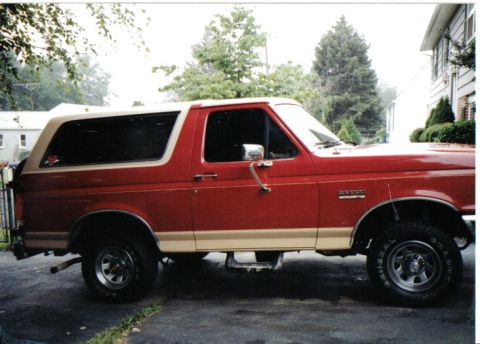 1990 Ford Bronco - A red 1990 Ford Bronco with a tan removable top is parked on an asphalt driveway.