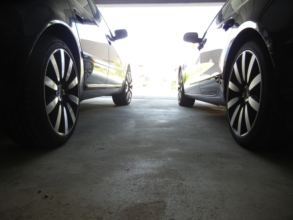 Two black cars with custom rims parked in a garage, viewed from the front wheel area