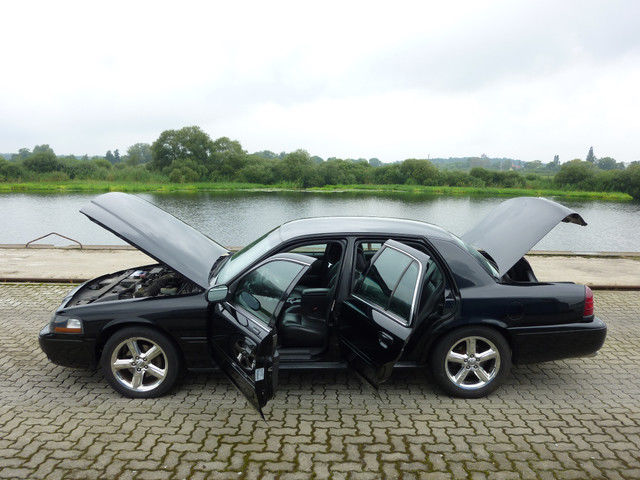 Black 2003 Mercury Marauder with all doors and hood open, parked by a body of water