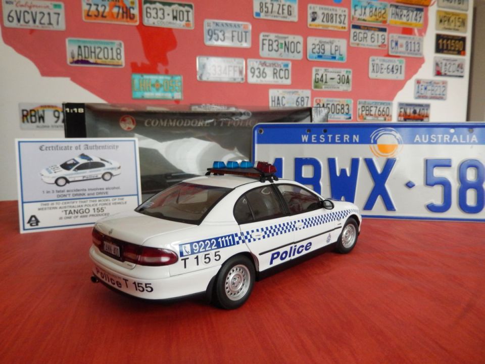 Die-cast model of a white police car with blue lights and checkered stripes, labeled 'Police T 155'. A certificate of authenticity is to its left