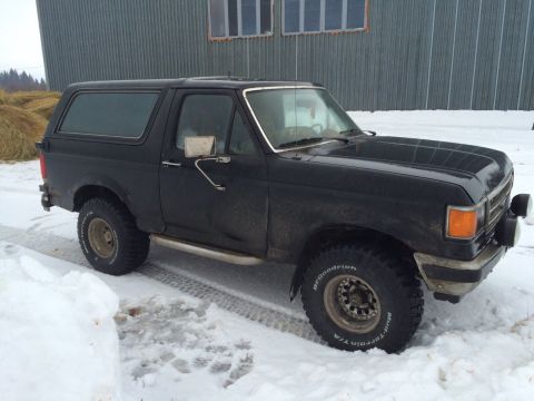 1987 Ford Bronco - A black 1987 Ford Bronco sits in a snowy landscape, appearing ready for off-road conditions.