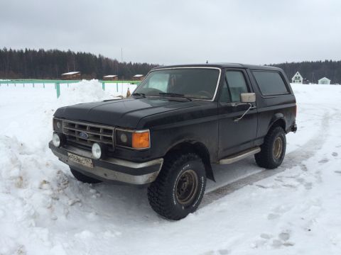 1987 Ford Bronco - A black 1987 Ford Bronco sits in a snowy landscape with trees in the background.