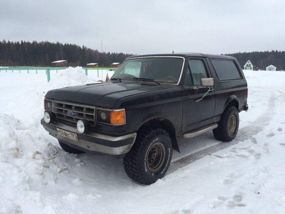 Black 1987 Ford Bronco parked in snow. Front grille and headlights visible