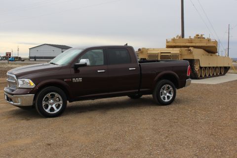 2015 Dodge 1500 - A Ram 1500 pickup truck is parked next to a large military tank in an outdoor lot.